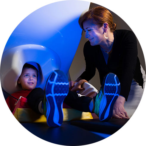 Child sits in MEG scanner with researcher assisting