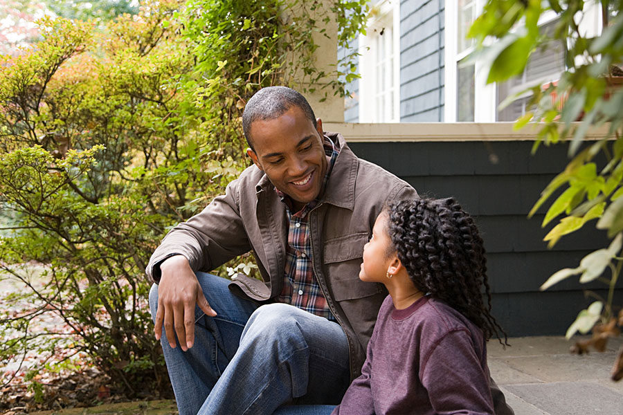 Father and young daughter sitting on a porch talking