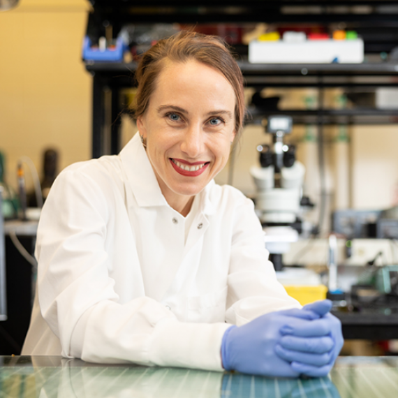 Woman sitting with hands folded on lab bench.