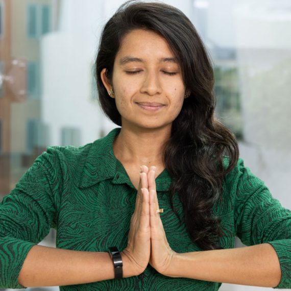 A woman with eyes closed and hands clasped in front of her body.