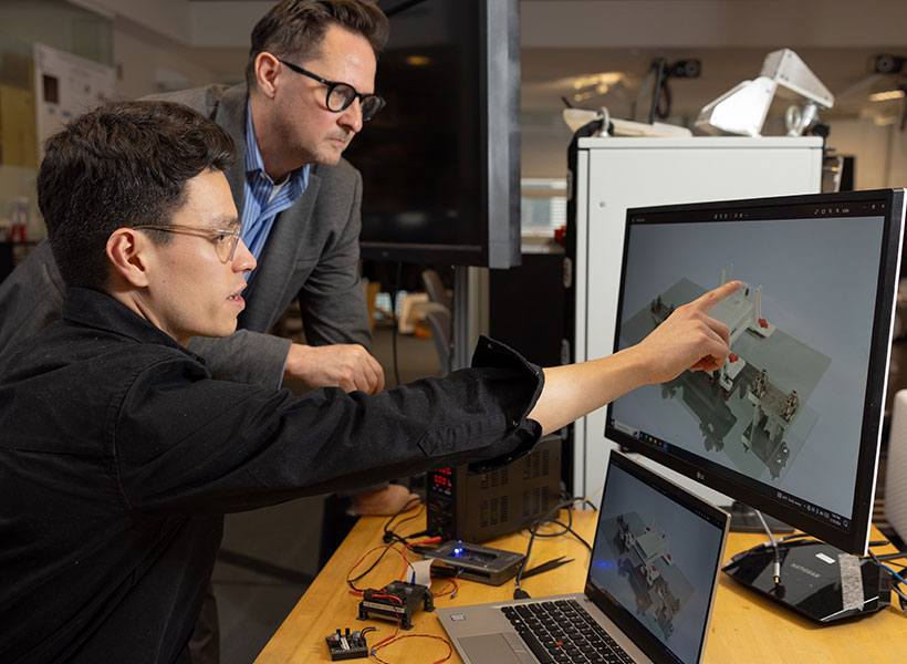 TWo men looking at a computer screen, one points to the image on the screen. 