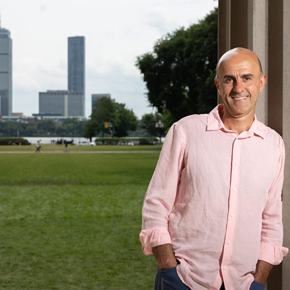 Man leaning against MIT column with Boston skyline in background.