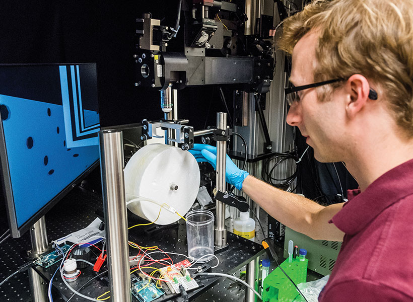 A scientist looks at a computer monitor and adjusts a small wheel. 