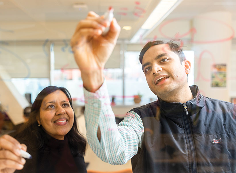 Two scientists write equations on a glass wall with a marker.