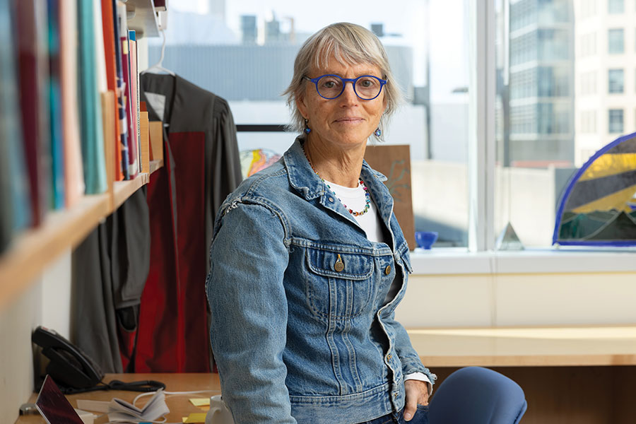 Female researcher leaning against desk with window in background.