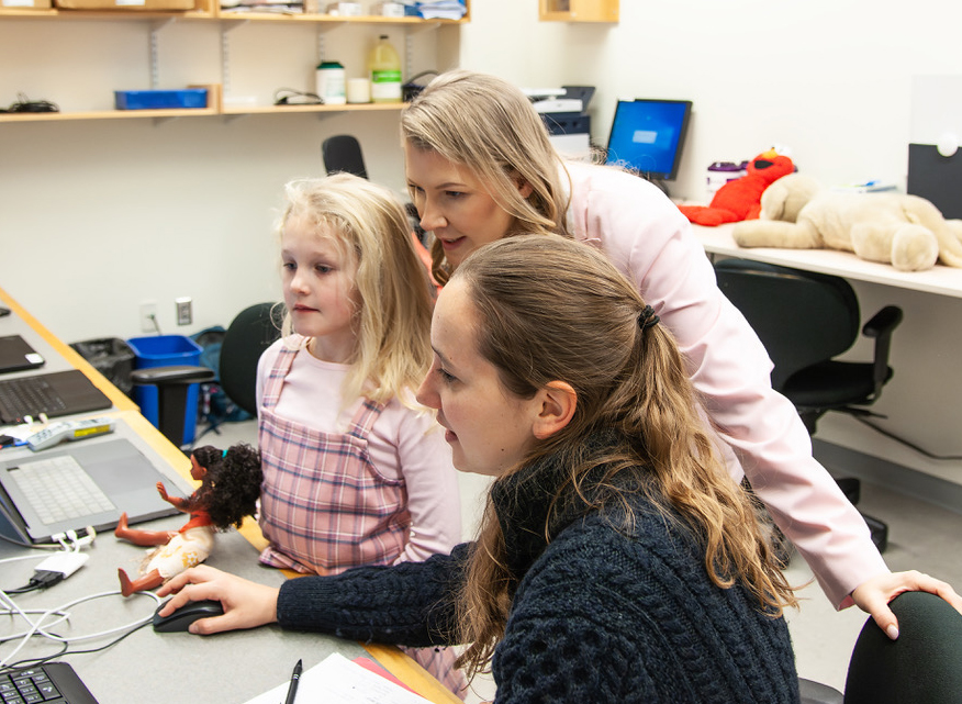 Two women and one child looking at a computer screen.